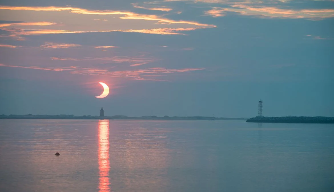 A partial solar eclipse is seen as the sun rises behind the Delaware Breakwater Lighthouse, Thursday, June 10, 2021, at Lewes Beach in