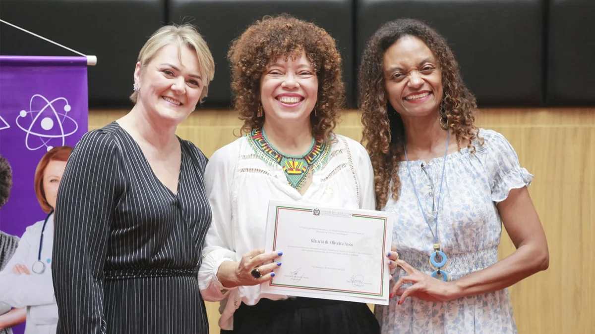 Glaucia Oliveira Assis, cientista valadarense, recebe homenagem na Assembleia Legislativa de Santa Catarina 1 Glaucia Assis, segurando o diploma de reconhecimento da ALESC, junto com as deputadas Luciane Carminatti (esquerda) e Vanessa Rosa (direita)