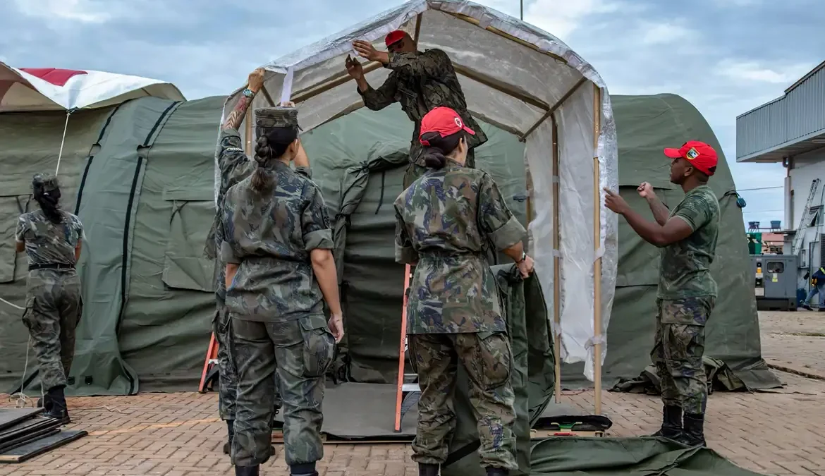 A foto mostra uma equipe do Exército Brasileiro montando as estrutura do hospital de campanha. A equipe veste uniforme camuflado