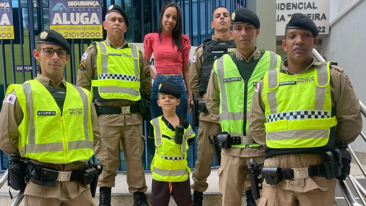 O pequeno Soldado Paradelo, de colete e boina da PM. Logo atrás, sua mãe Rafaela Paradelo, junto com a equipe de policiais militares,