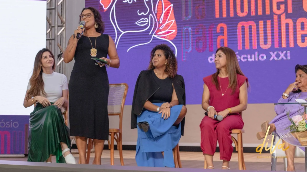 A delegada Adeliana Xavier, de vestido preto, falando durante o seminário